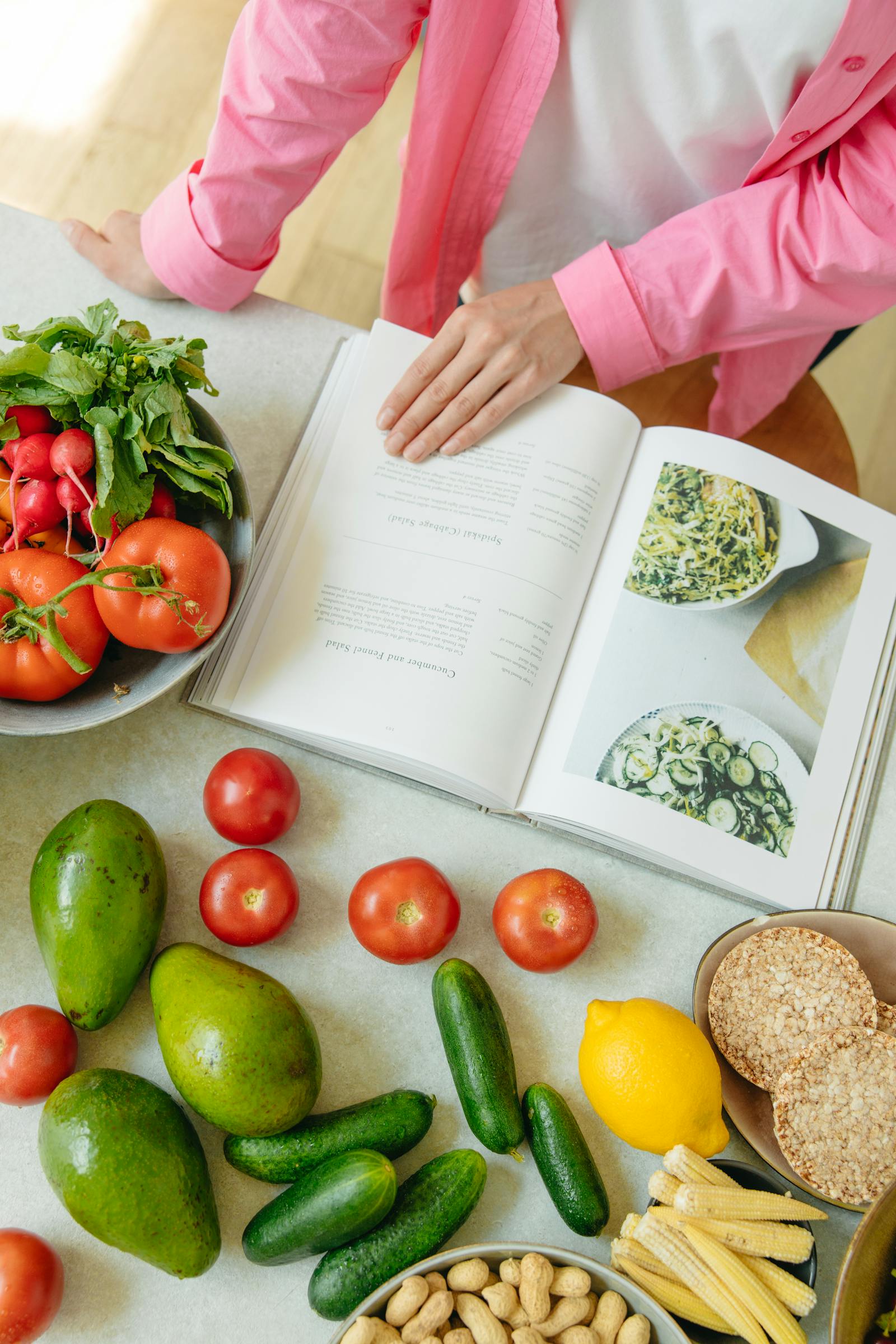 Fresh cookbook ingredients arranged on a table with vegetables, olive oil, and plated food.
